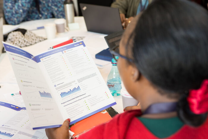 A woman looks at a bi-fold pamplet displaying charts and graphs while sitting at a table holding a cup of coffee.