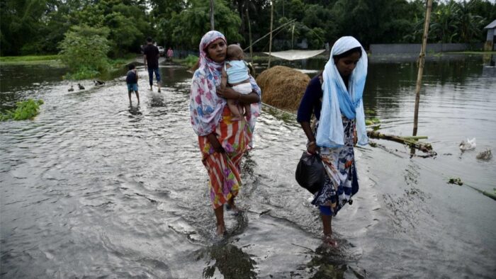 Deux femmes pataugeant dans l’eau, l’une tenant un bébé.